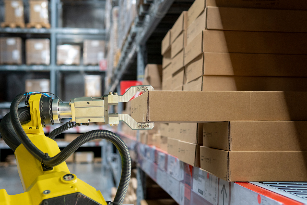 yellow robotic arm carrying cardboard box in warehouse